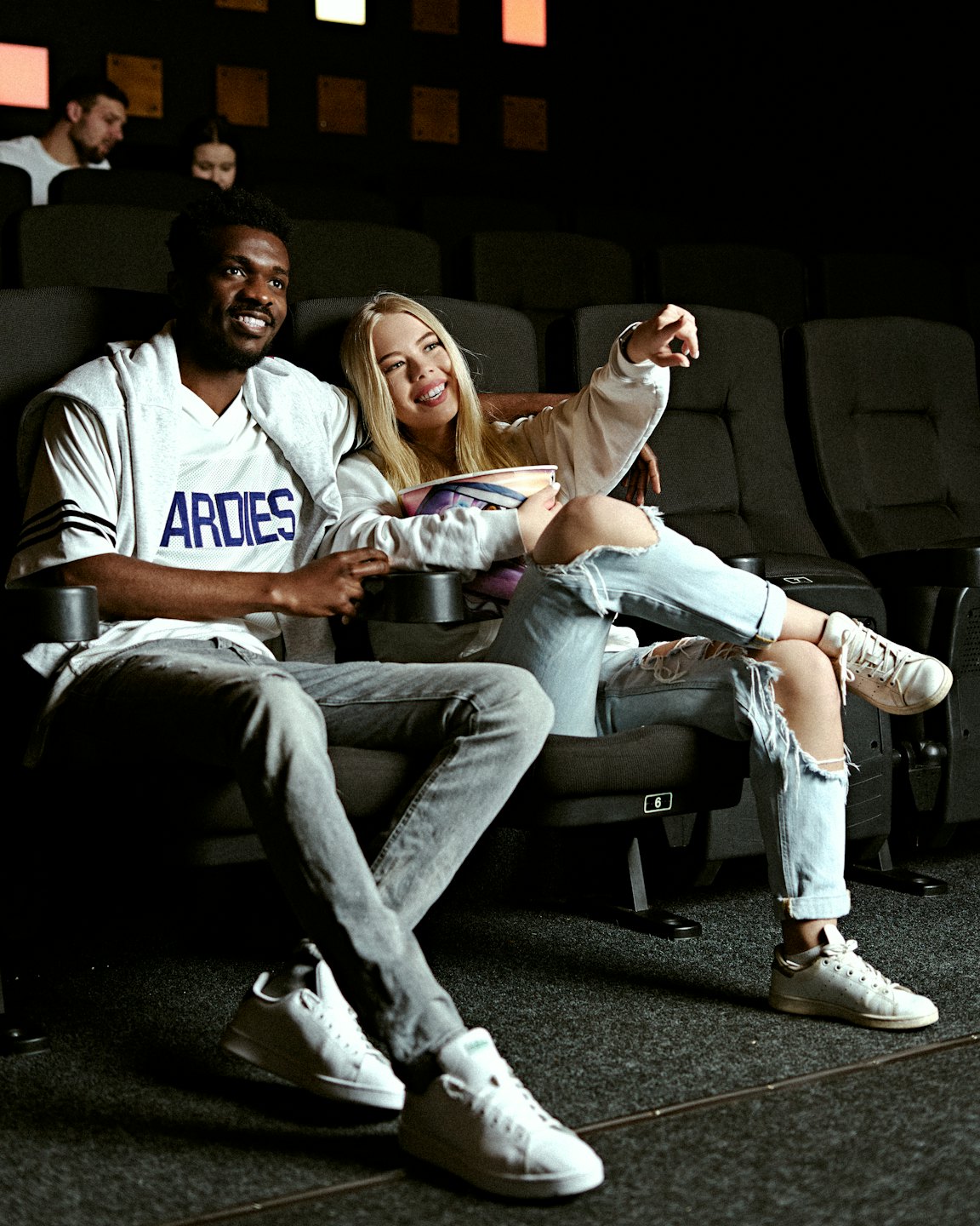 Giovane coppia sorridente in un cinema buio con popcorn.