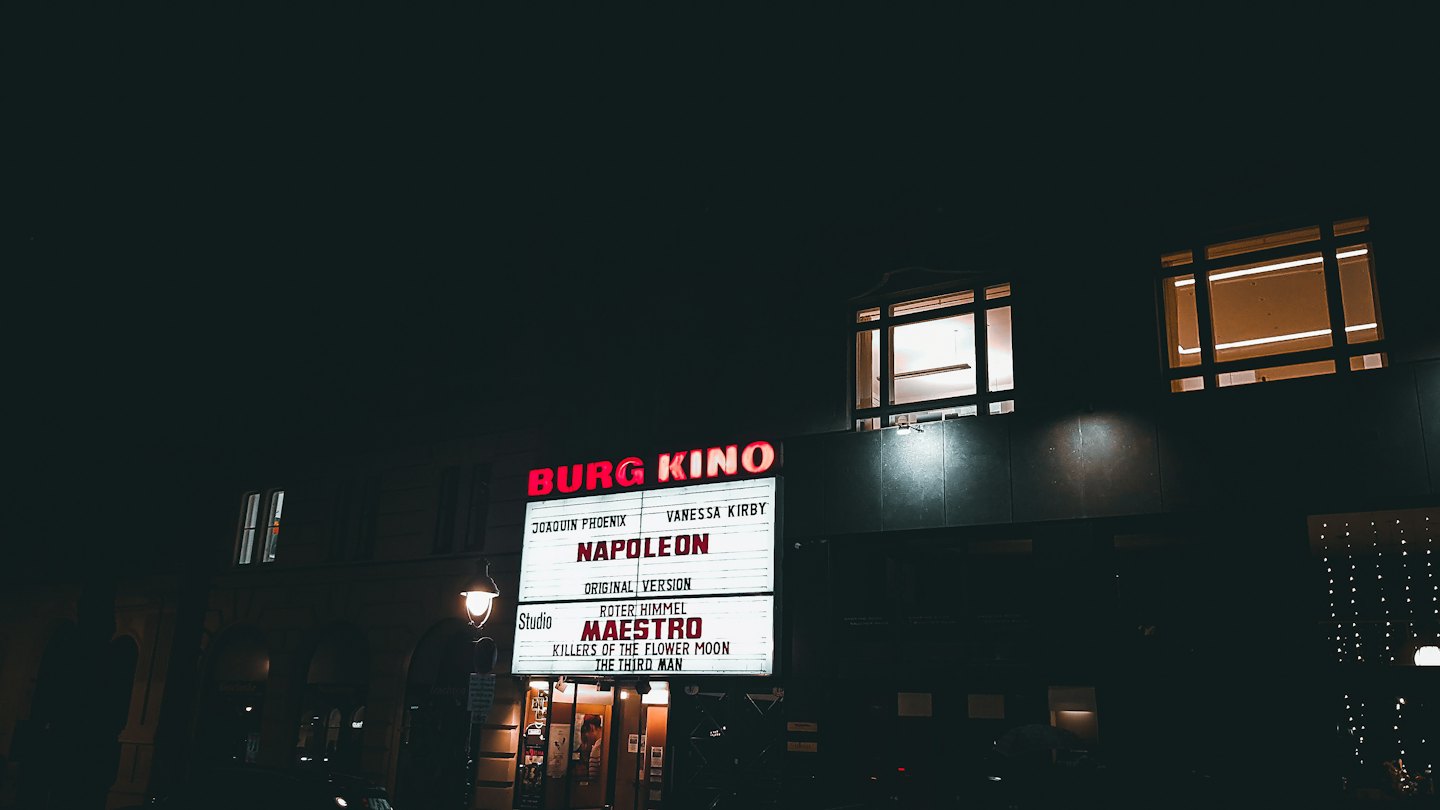 Insegna luminosa di un cinema con titoli di film sopra il marciapiede.