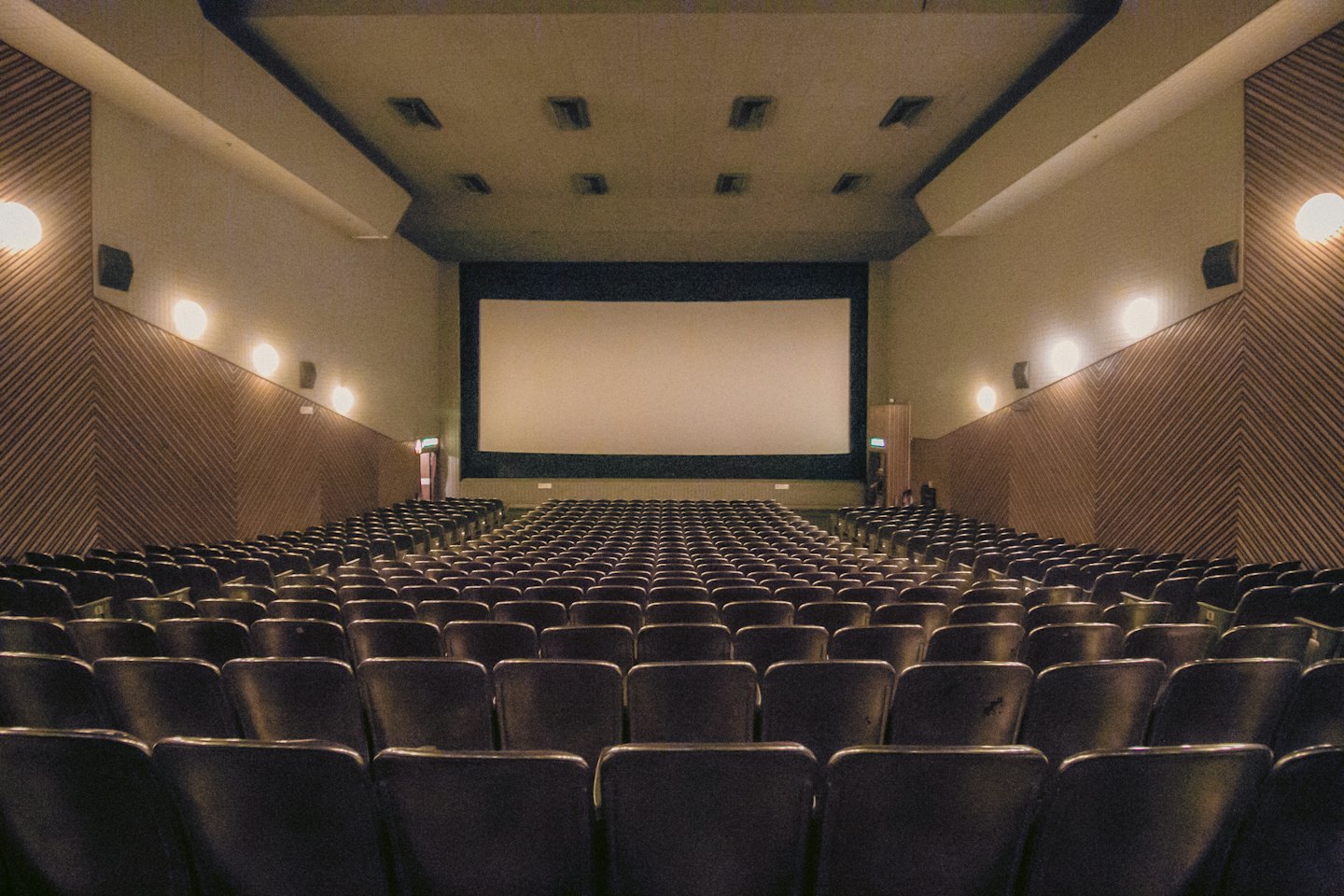 Sala cinematografica vuota con file di poltrone di fronte a uno schermo bianco.